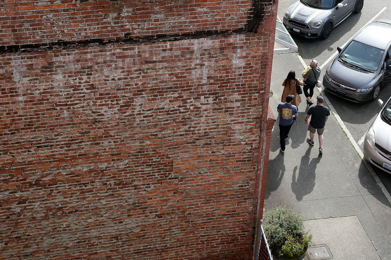 Pedestrians walk beside a brick building on Wetmore Avenue on March 17, 2021, in Everett, Washington. Old buildings constructed before 1945, with unreinforced masonry, are vulnerable to seismic waves. The exterior could break away and plummet into the street. (Andy Bronson / The Herald)