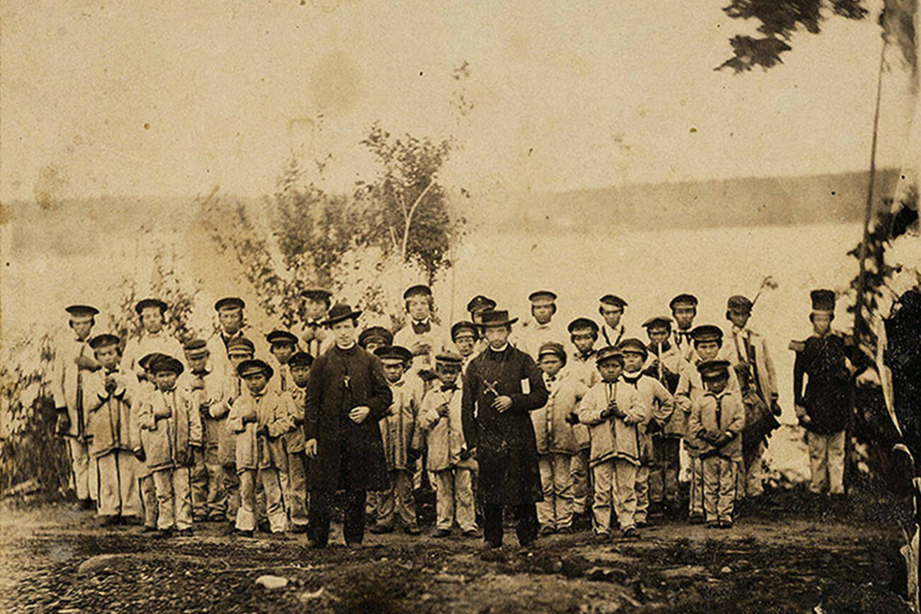 Rev. Eugene Casimir Chirouse, pictured here holding a cross at front right in 1865, founded a boarding school for Indigenous students on Tulalip Bay. It became one of the first religious schools in the country to receive a federal contract to educate Indigenous youth, with the goal of assimilation. (Courtesy of Hibulb Cultural Center)