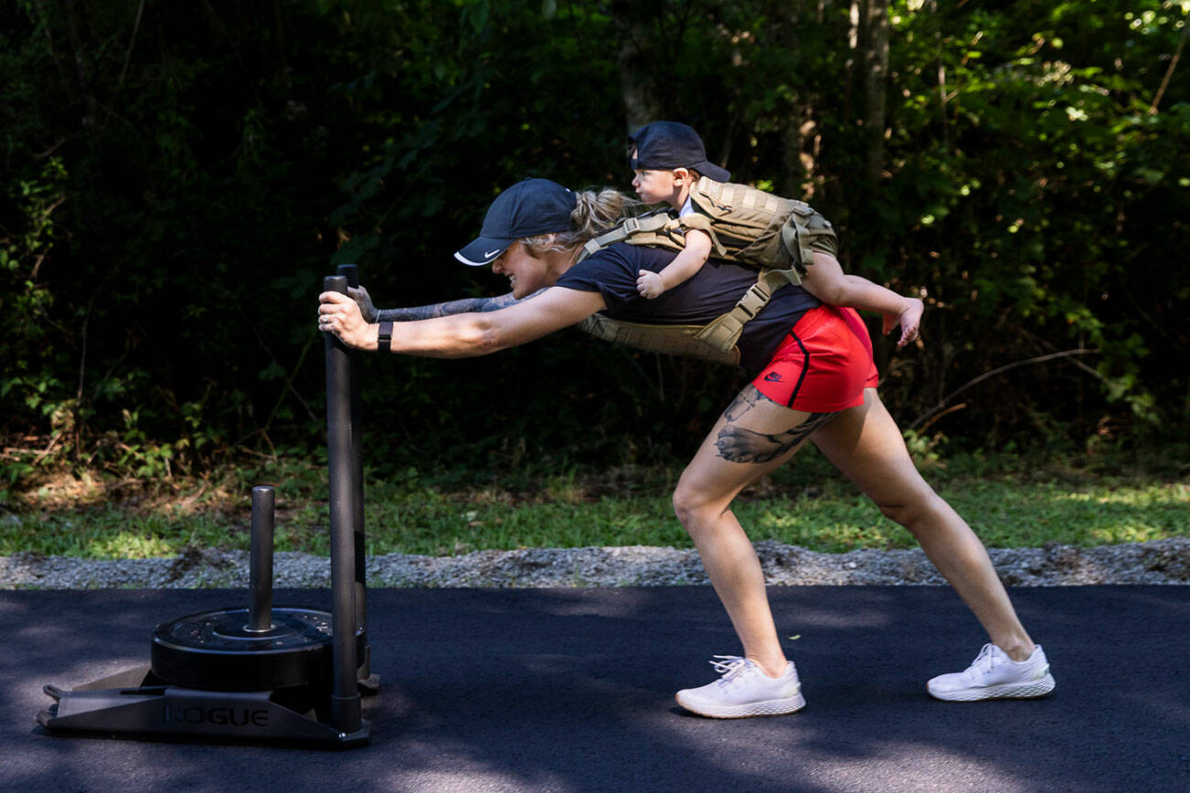 A few weeks before what could be her final professional UFC fight, Miranda Granger grimaces as she pushes a 45-pound plate up her driveway on Tuesday, July 12, 2022, in Lake Stevens, Washington. Her daughter Austin, age 11 months, is strapped to her back. (Olivia Vanni / The Herald)