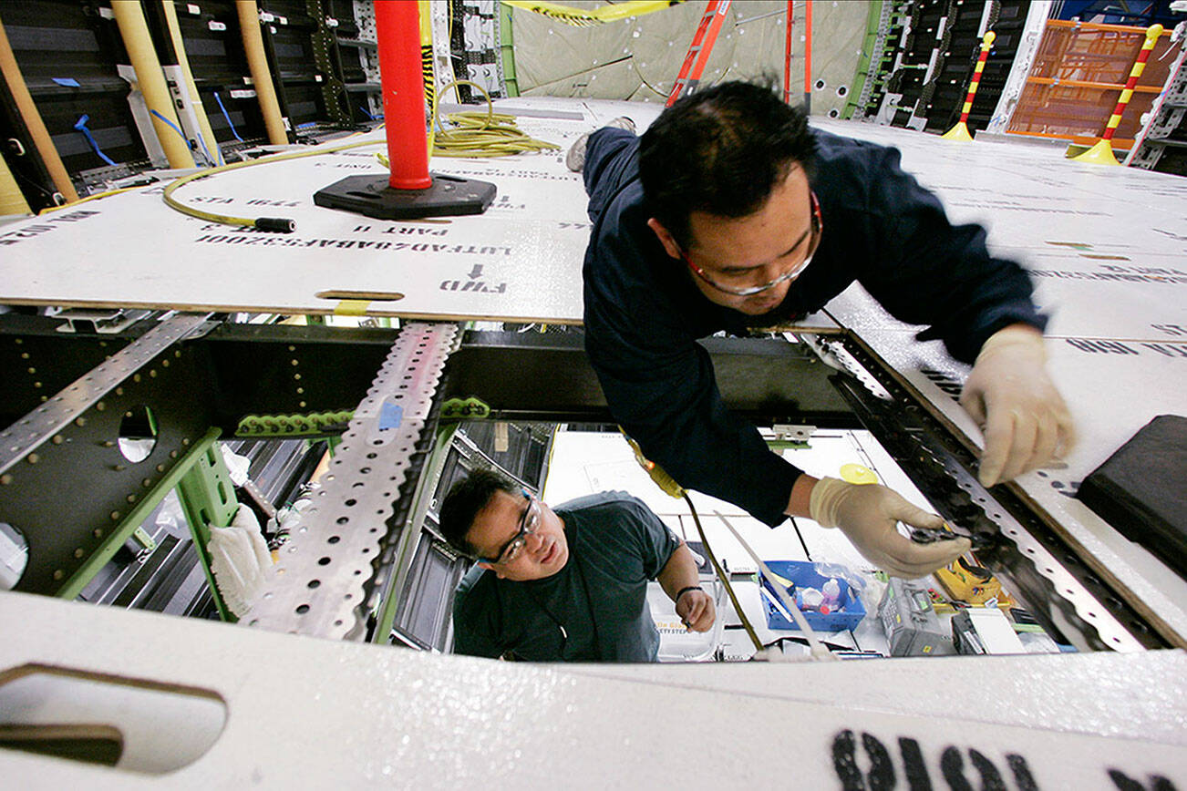 One worker looks up from the cargo area as another works in what will be the passenger compartment on one of the first Boeing 787 jets as it stands near completion at the front of the assembly line, Monday, May 19, 2008, in Everett, Wash. The plane, the first new Boeing jet in 14 years, is targeted for power on in June followed by an anticipated first flight sometime late in 2008.  (AP Photo/Elaine Thompson)