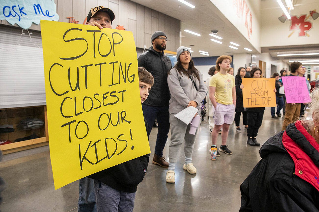 Grayson Huff, left, a 4th grader at Pinewood Elementary, peaks around his sign during the Marysville School District budget presentation on Tuesday, Nov. 28, 2023 in Marysville, Washington. (Olivia Vanni / The Herald)