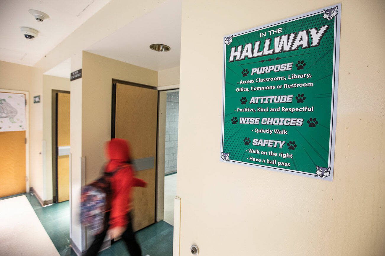 A student walks down a hallway at Evergreen Middle School past a sign displaying different values the students should embody while occupying the space on Friday, Jan. 26, 2024 in Everett, Washington. (Olivia Vanni / The Herald)