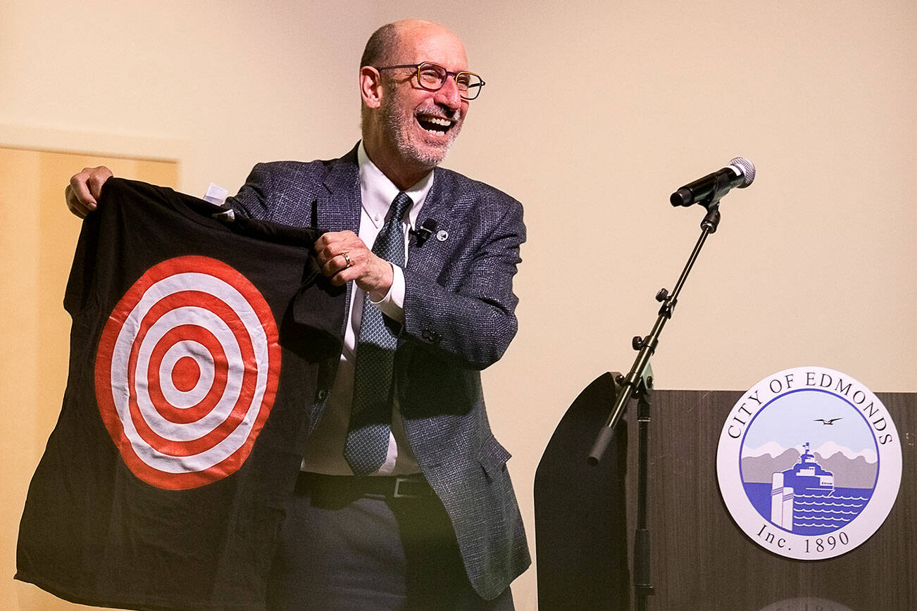 Edmonds Mayor Mike Rosen is reflected in a countertop as he pulls out a bullseye shirt at the start of his 2025 budget presentation at the Edmonds Waterfront Center on Tuesday, Oct. 1, 2024 in Edmonds, Washington. (Olivia Vanni / The Herald)