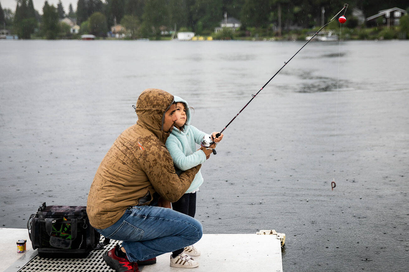 Ridley Biggs, 5, right, learns how to cast with her father Mike Biggs as it starts to rain on Friday, June 17, 2022 in Lake Stevens, Washington. (Olivia Vanni / The Herald)