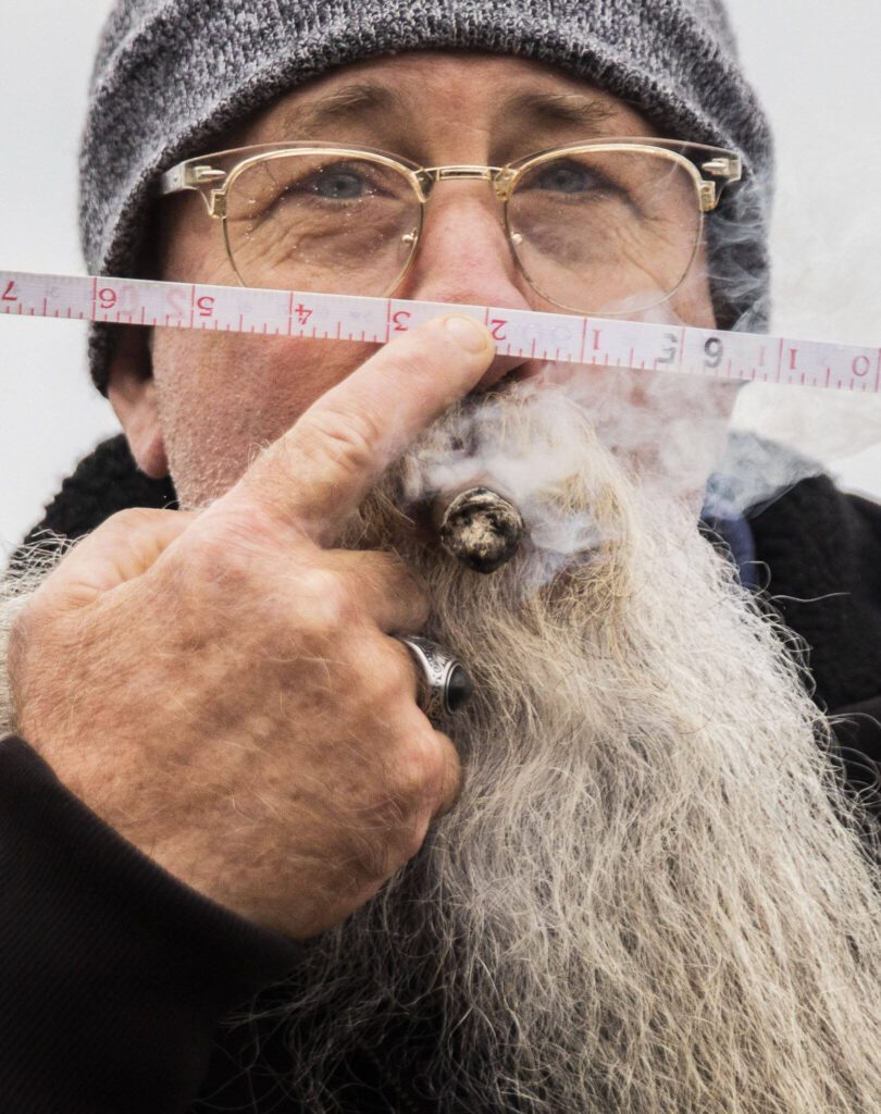 Jeff Raye smokes a cigar while he holds a tape measure to his nose during the Guinness World Record Beard Chain Attempt on Friday, Nov. 1, 2024 in Everett, Washington. (Olivia Vanni / The Herald)
