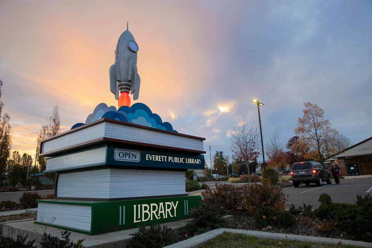 The sun sets beyond the the Evergreen Branch of the Everett Public Library as a person returns some books on Friday, Nov. 11, 2022, in Everett, Washington. (Ryan Berry / The Herald)