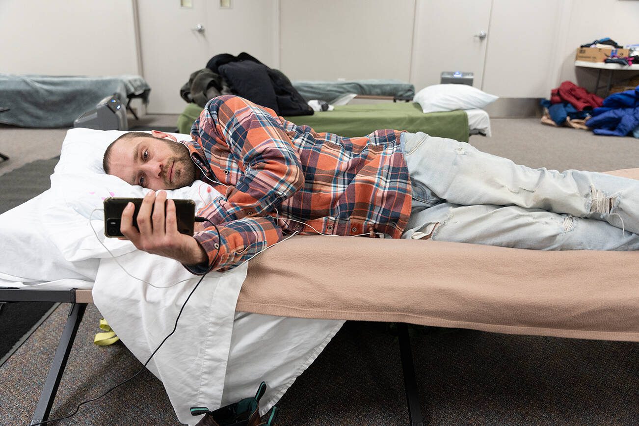 Justin Roeth lies on a bed on Monday, Dec. 2 at the Marysville Cold Weather Shelter in Marysville, Washington. (Will Geschke / The Herald)