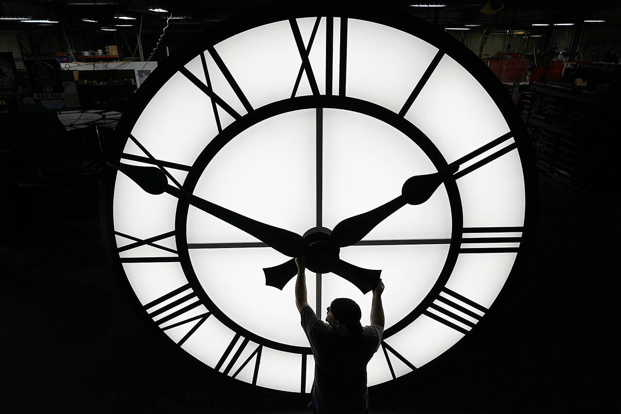 Electric Time technician Dan LaMoore adjusts a clock hand on a 1,000-pound, 12-foot diameter clock built for a resort in Vietnam, in March 2021, in Medfield, Mass. A bill before the Washington state Legislature could make standard time permanent in Washington, ending the twice-yearly switch between standard time and daylight saving time. (Elise Amendola / Associated Press file photo)