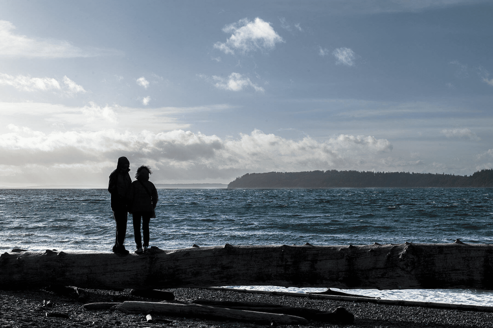 A couple stands on a large piece of driftwood in the wind at Mukilteo Lighthouse Park on Friday, Jan. 4, 2018 in Mukilteo, WA. There is a small craft advisory in effect until 10 pm Friday. (Olivia Vanni / The Herald)